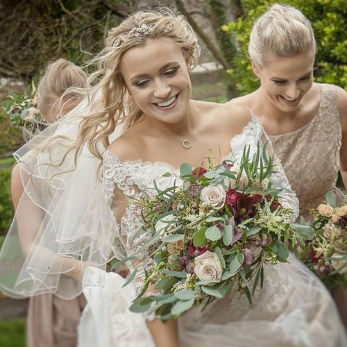 Beautiful bride with long blonde wavy hair, holding a bouquet of cream and burgundy roses.